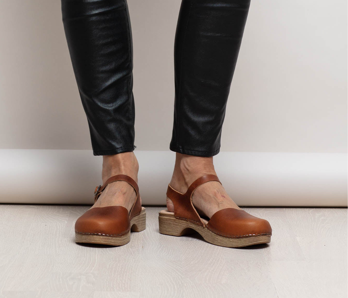 Brown Mary Jane clogs worn with black leather pants on a neutral background