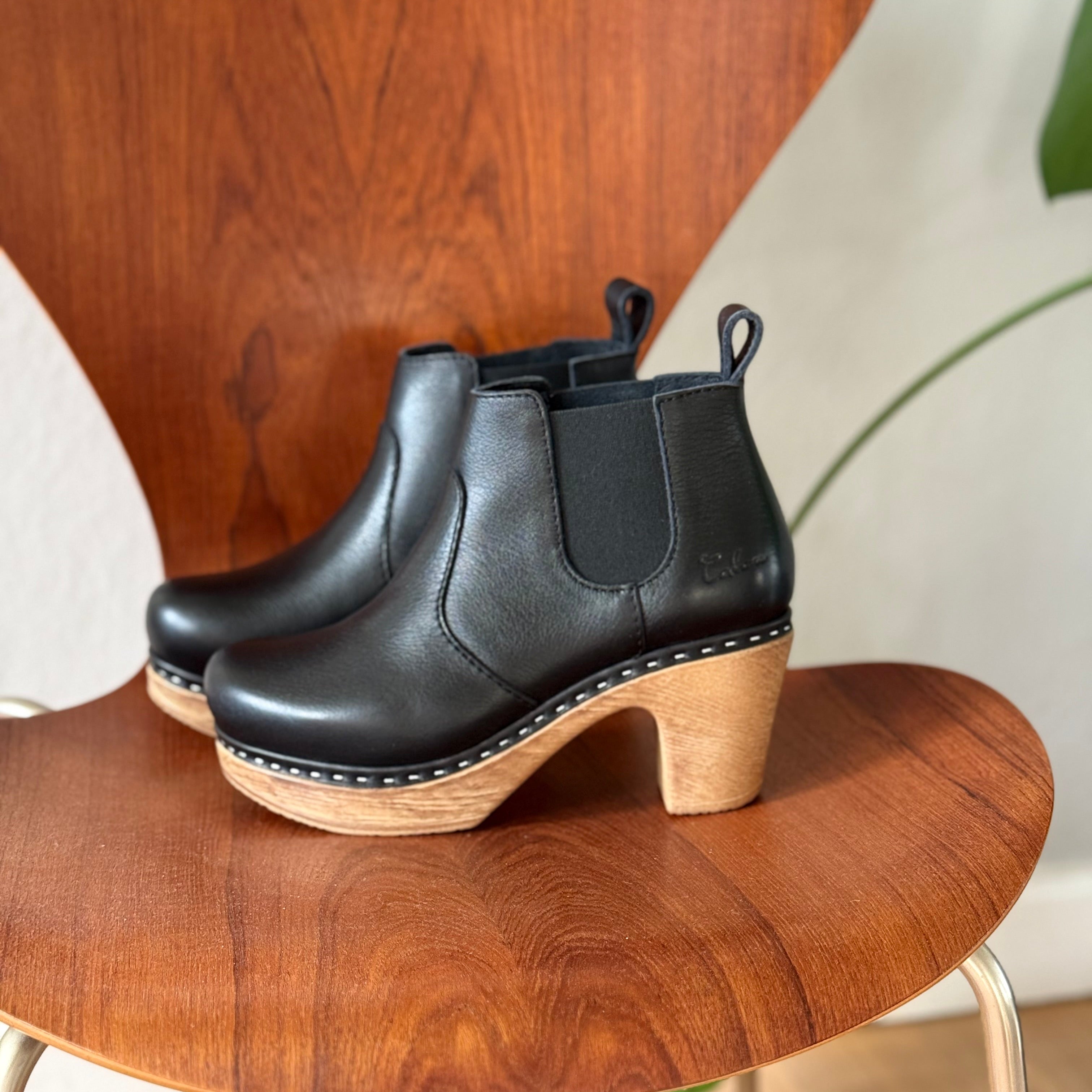 Black ankle boots with wooden soles on a brown chair