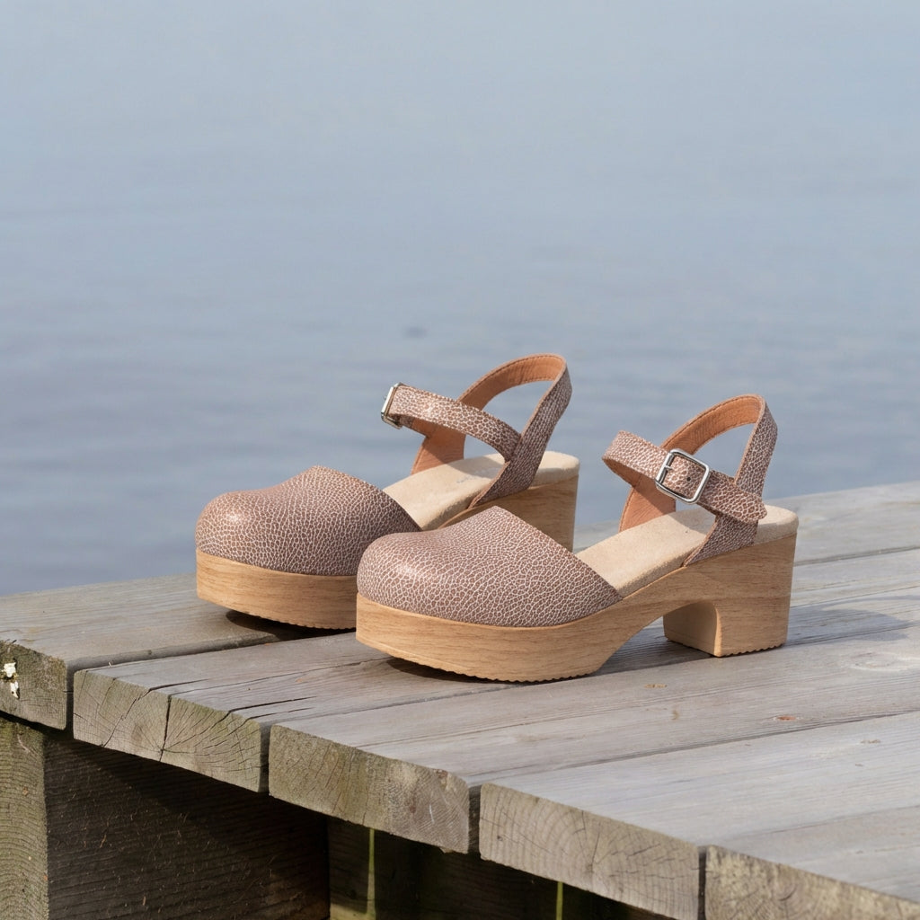 Calou Sara crackel leather Mary Jane clogs on a dock by a body of water.